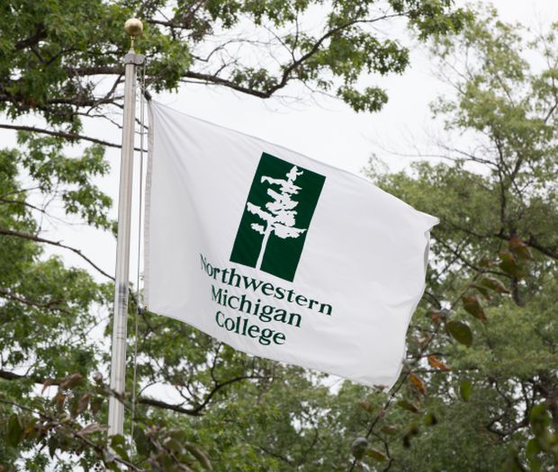 NMC flag on a flag pole with trees in the background