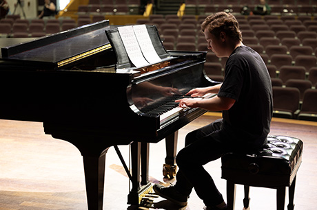 A Music program student at a piano in an NMC concert space