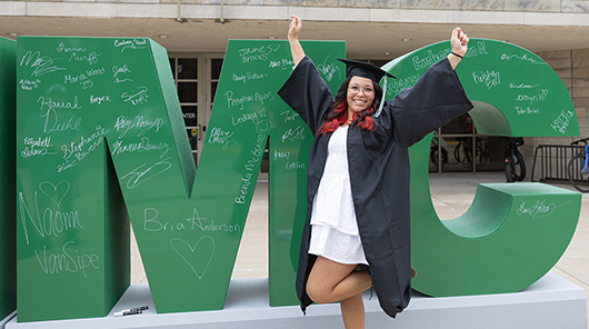 An NMC graduate poses in her cap and gown in front of the Dennos Museum Center