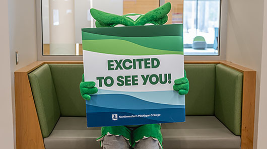 NMC's new mascot, Swoop, behind a sign that reads Excited to See You