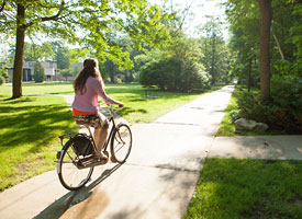An international student bikes along a sidewalk on NMC's main campus