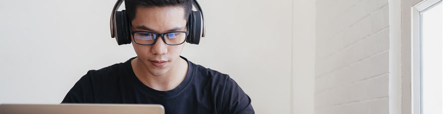 Photo of a student behind a laptop wearing headphones