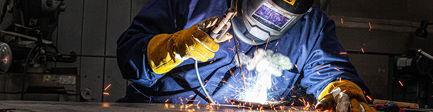 An NMC welding program student in a welder's mask welding at a table