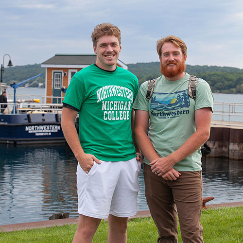 A photo of two Great Lakes Water Studies Institute students by the harbor on West Bay, with the research vessel Northwestern in the background