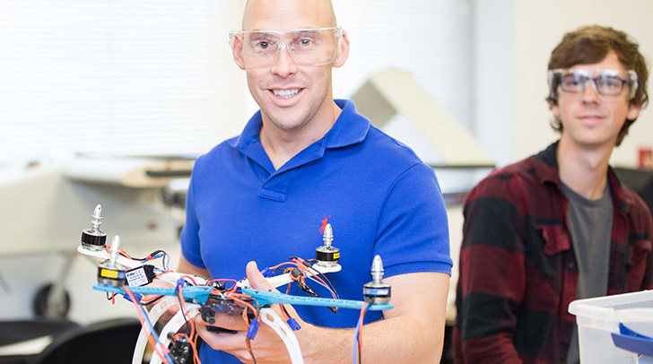 An NMC Aviation program instructor holds a small drone while a student looks on