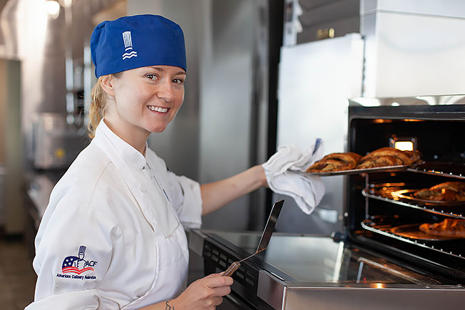 A Great Lakes Culinary Institute Baking Certificate program student pulls freshly baked croissants from an oven