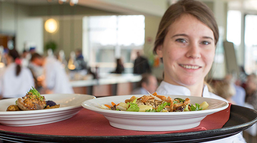 An NMC culinary program student delivers salads to a table at Lobdell's teaching restaurant